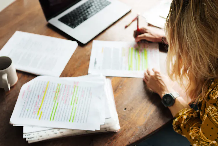 high angle of woman marking papers with laptop in background