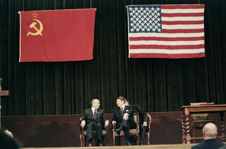 TYwo men sit under giant flags.