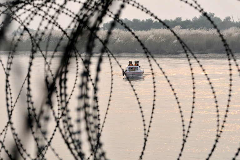 Barbed wire is seen in front of a small boat with people in it.