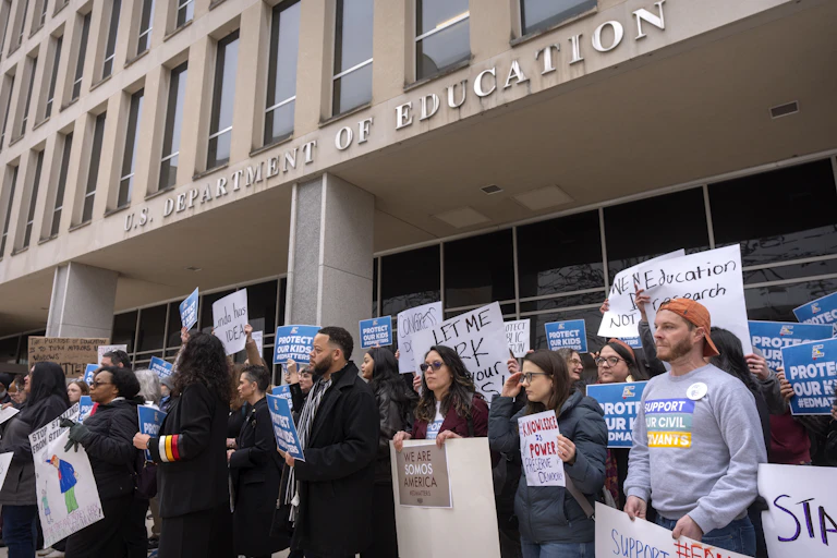 people carrying signs protest in front of a building labeled us department of education