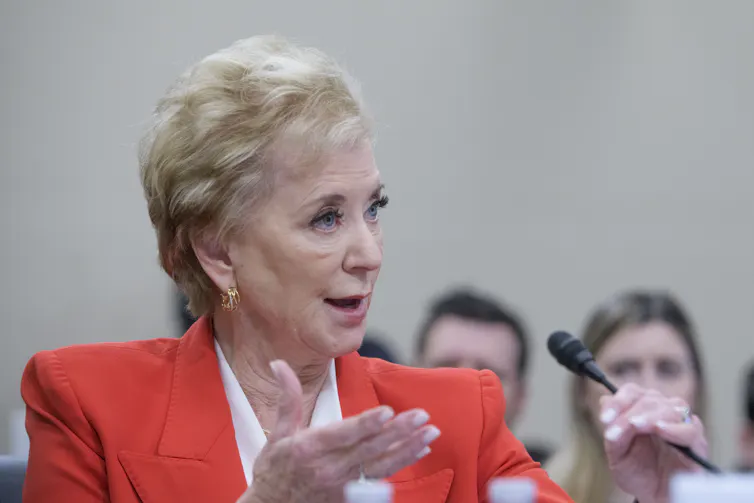 a woman wearing an orange jacket gestures in front of a microphone
