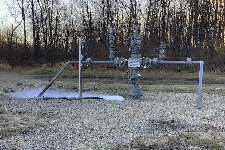 On a flat piece of ground with some pipes emerging from it, a cloud of vapor escapes from a pipe.