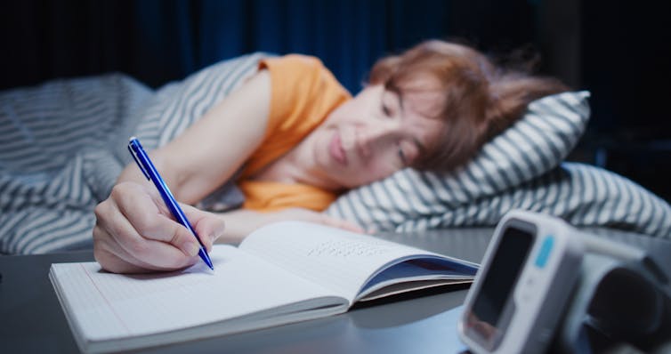 La mujer que acostada en la cama llega a la escritura de lápiz en el cuaderno