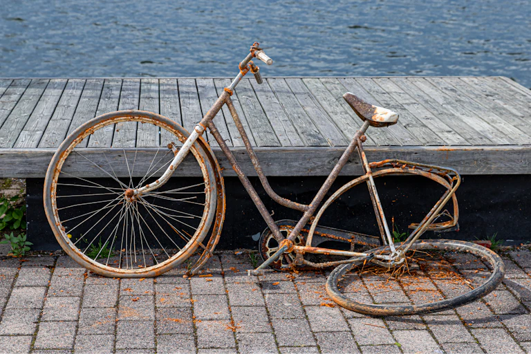An old, broken bicycle, resting on a dock near water