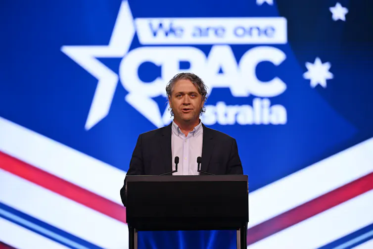 A man in a suit speaks at a podium on a big stage