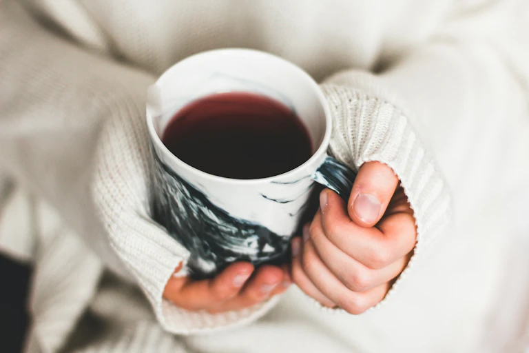 Woman wearing woolly jumper clutching hot cup of black tea