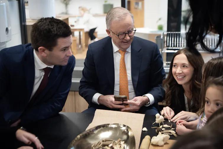 Two men and a woman smile and talk to children around a low table.