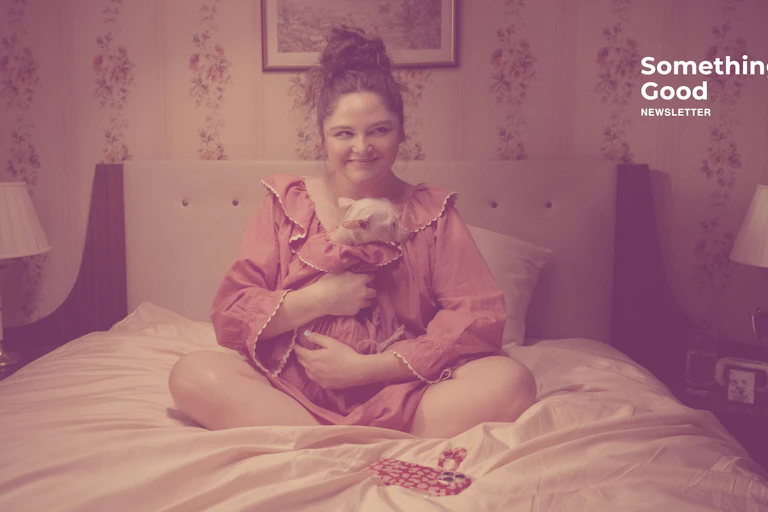 A woman sits on her bed holding a small dog.