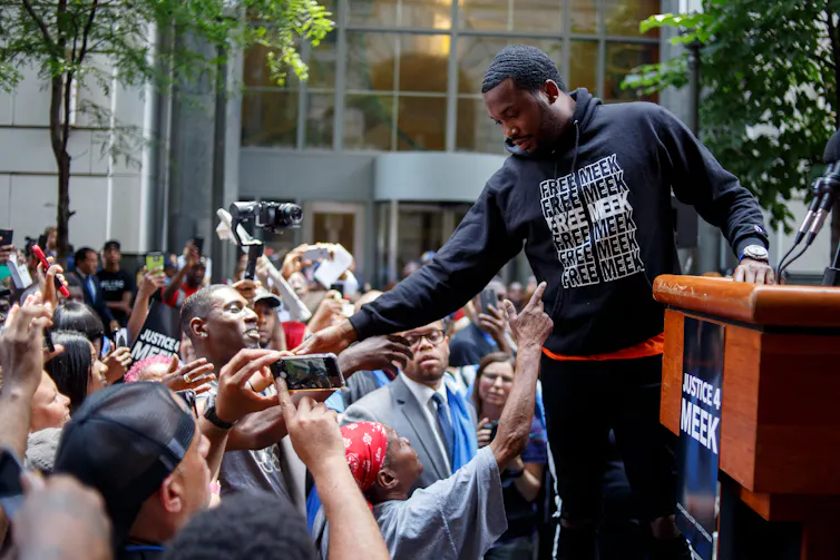Man in black hoodie that says 'Free Meek' interacts with crowd of supporters in street