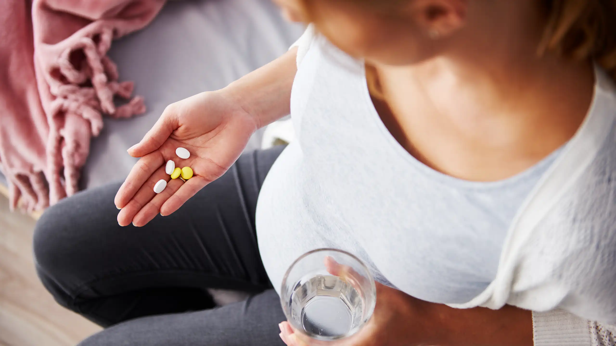 Top view of a pregnant person with a large belly looking down at a handful of vitamins.
