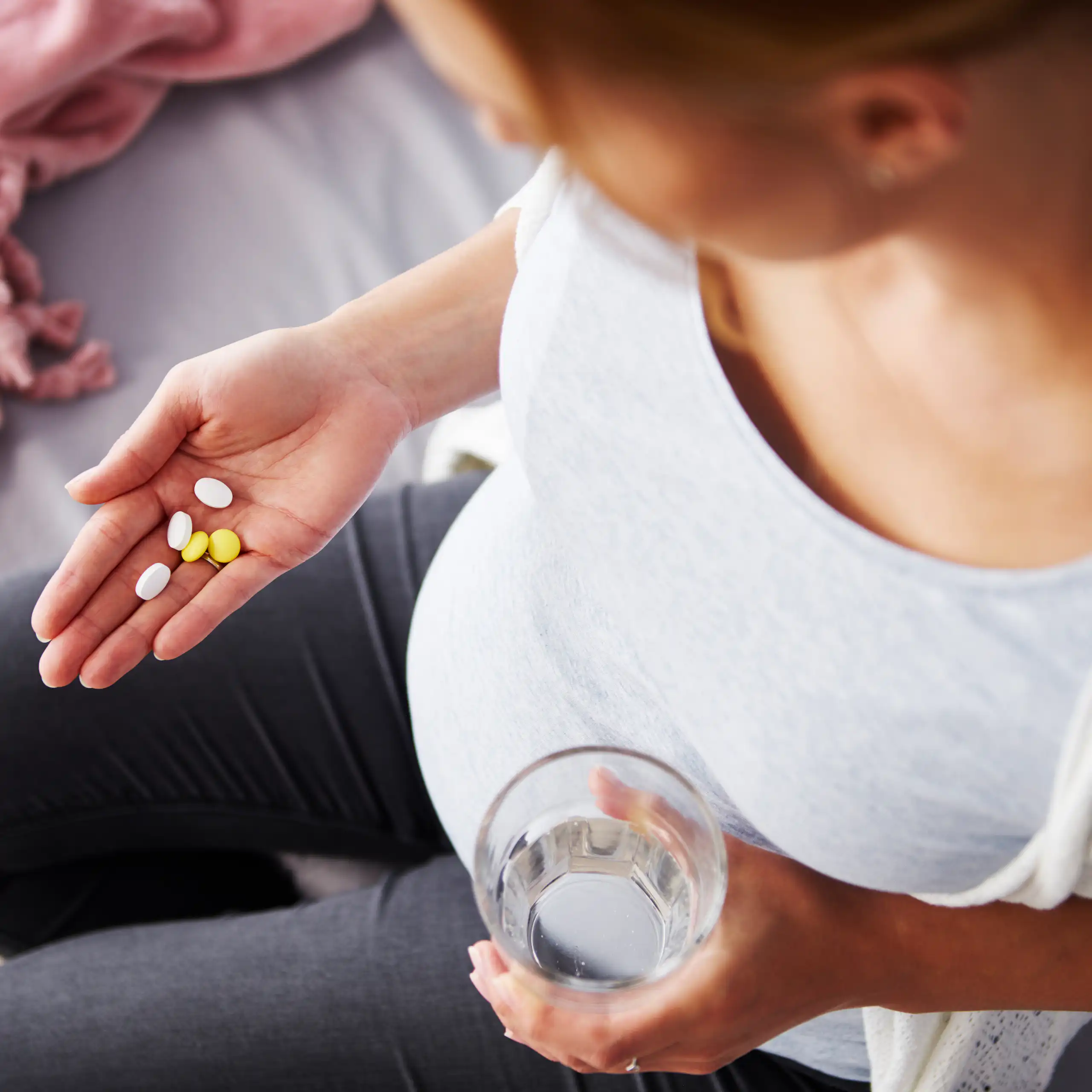 Top view of a pregnant person with a large belly looking down at a handful of vitamins.