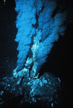 Tall clouds of smoke rising from rocks in the ocean.