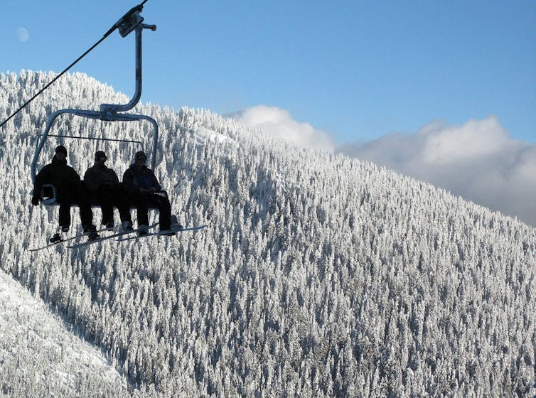 Tres personas en los teleféricos Silhetizadas en árboles de madera y cielo azul cubiertos de nieve y cielo azul