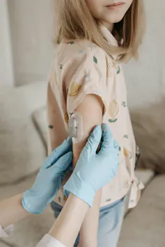 A gloved hand examining a glucose monitor on a girl's arm.