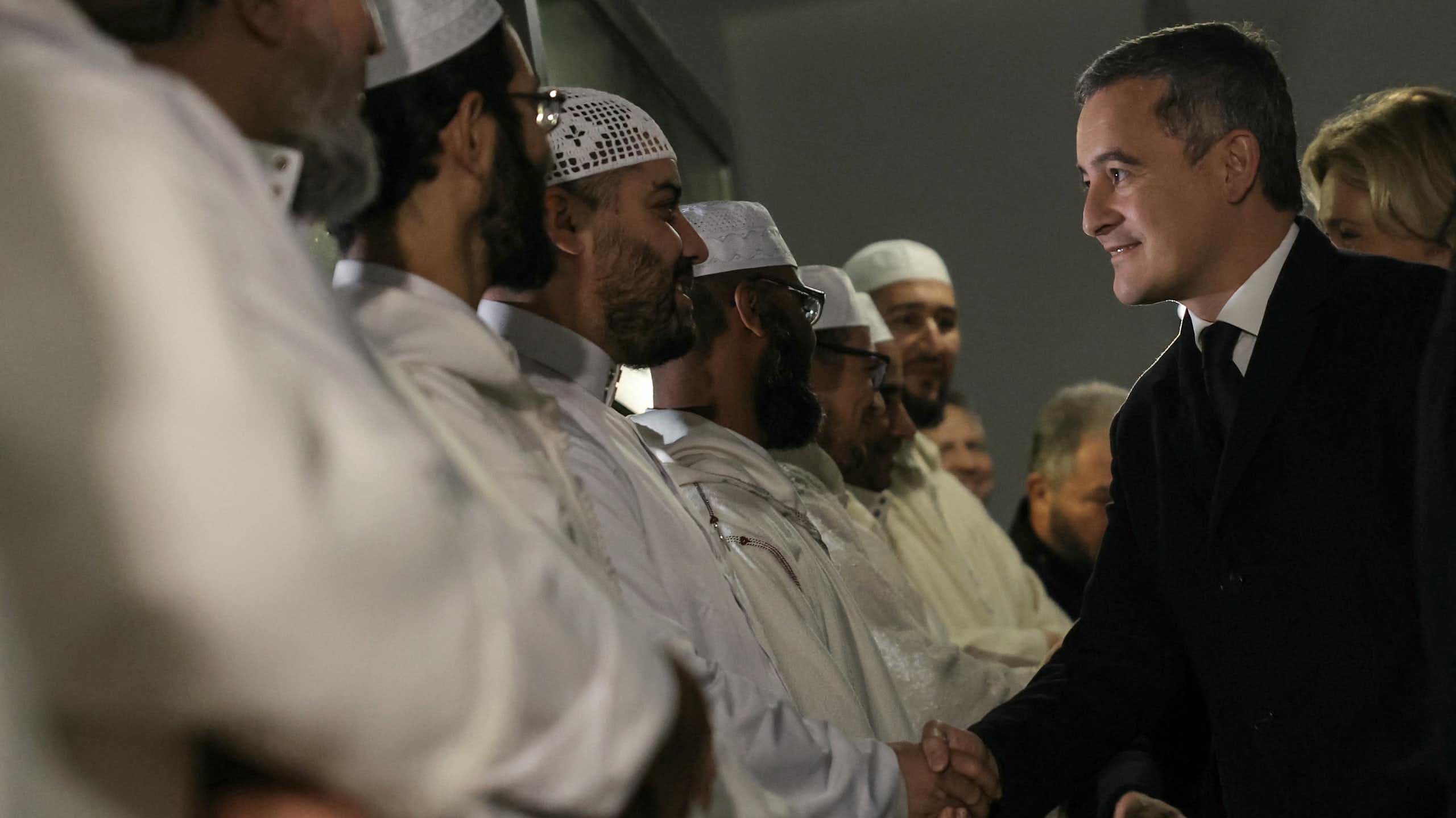 Gérald Darmanin sert la main à un groupe d'imams.