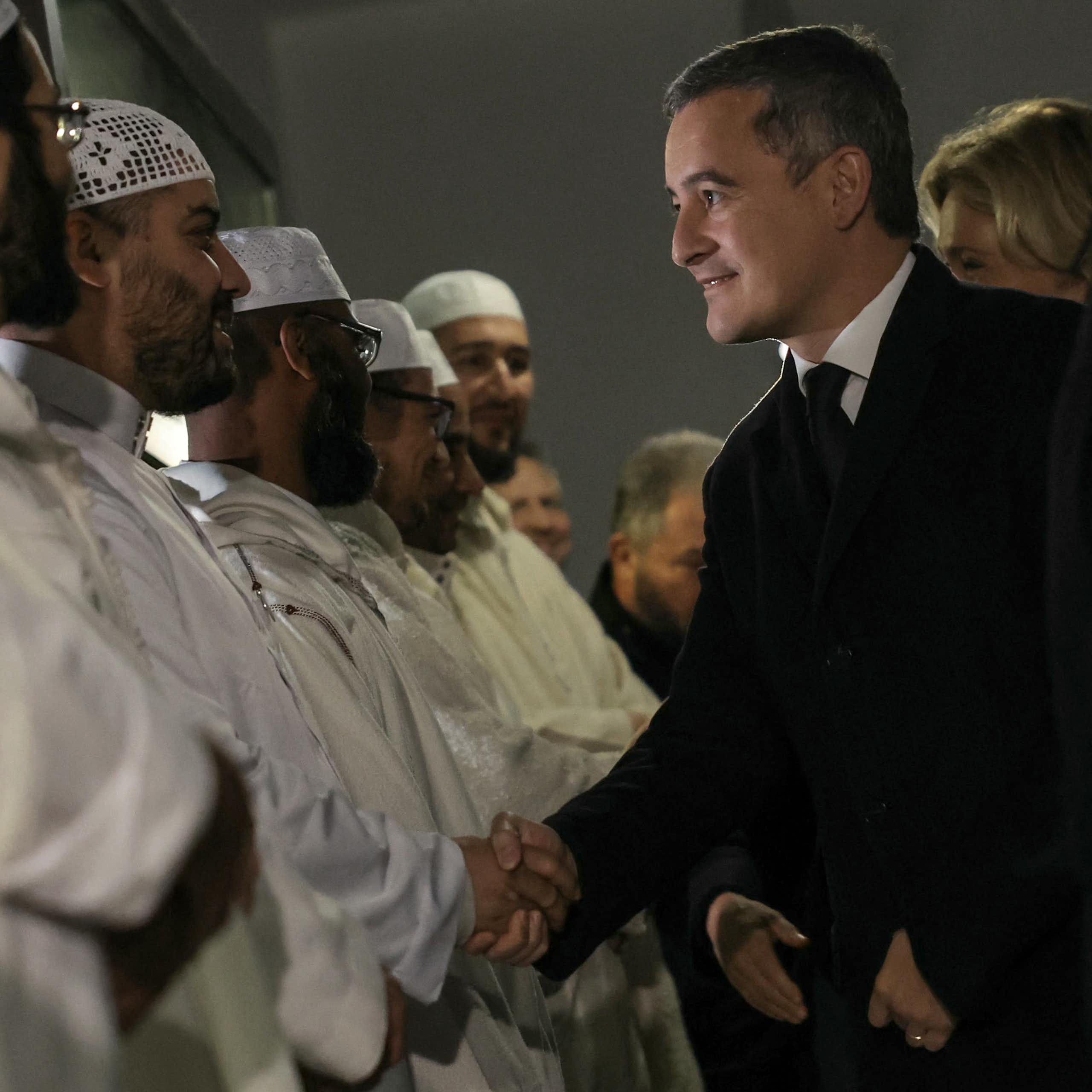 Gérald Darmanin sert la main à un groupe d'imams.