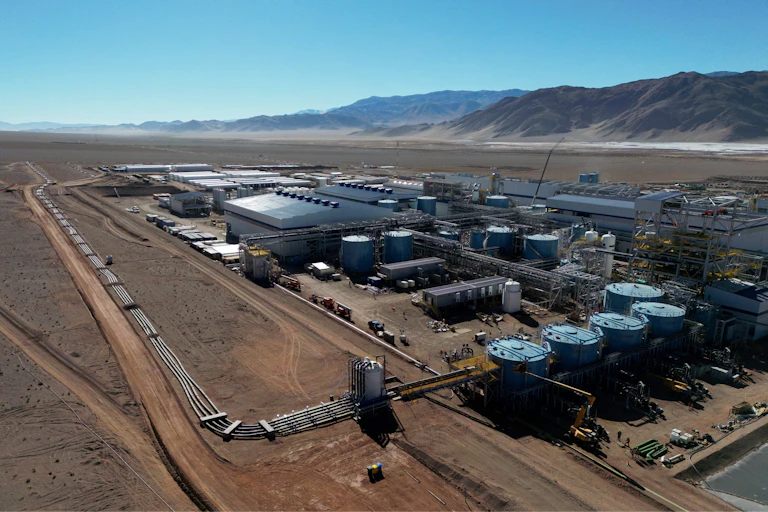 An aerial view of industrial buildings in a desert-like landscape with what appear to be mountains in the distance.