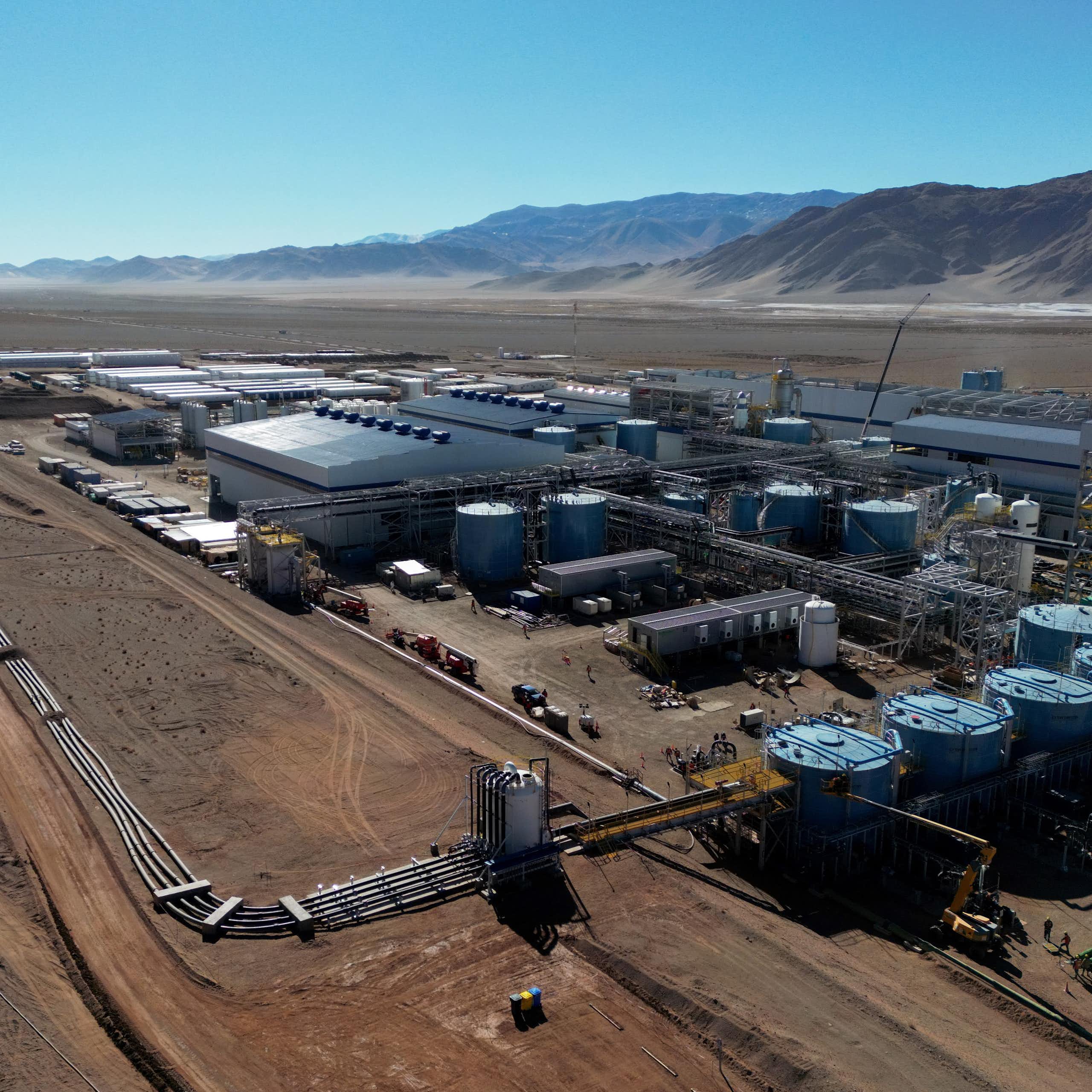 An aerial view of industrial buildings in a desert-like landscape with what appear to be mountains in the distance.
