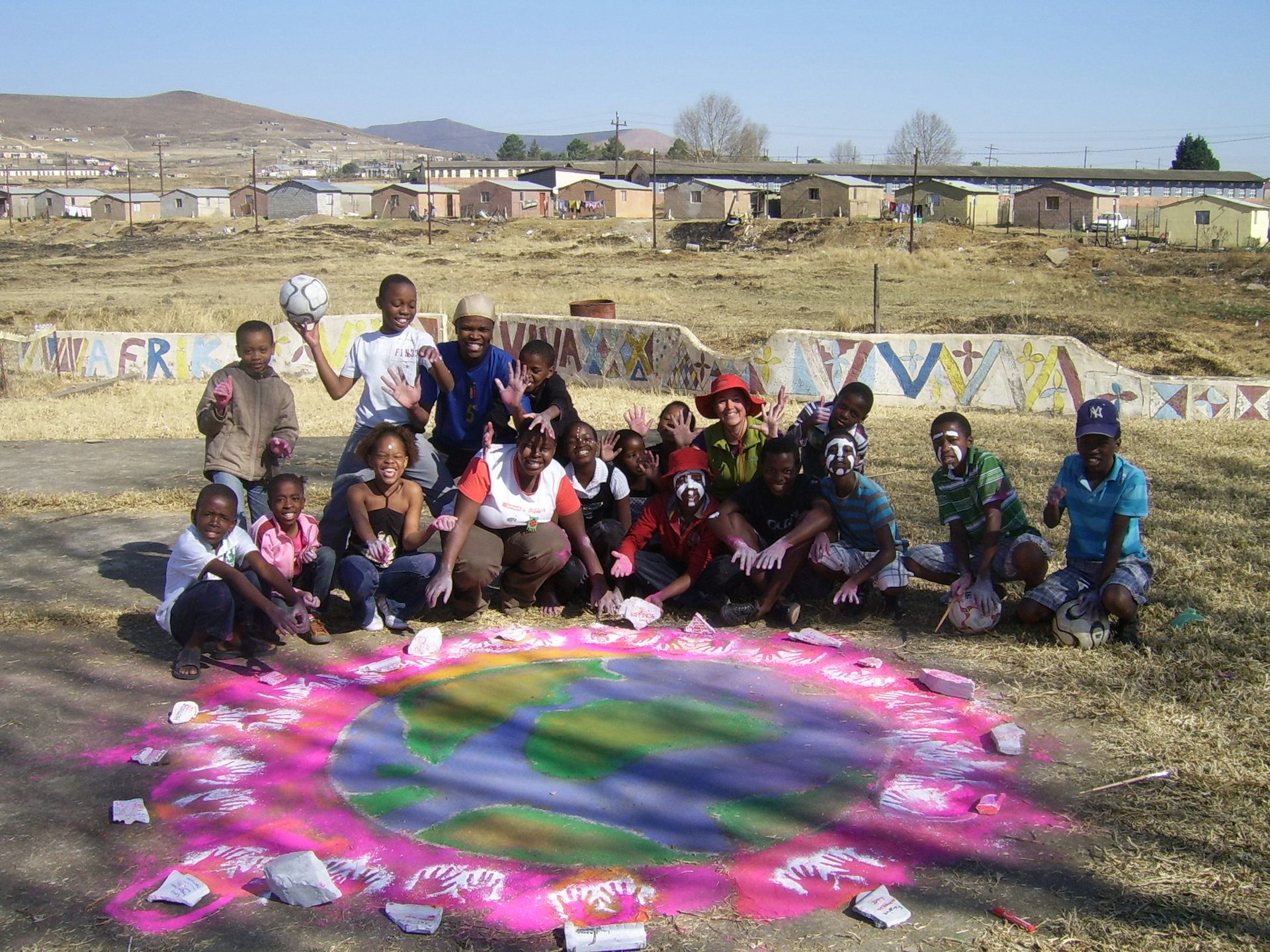 Children sit on the ground around a big pink circle drawn in chalk