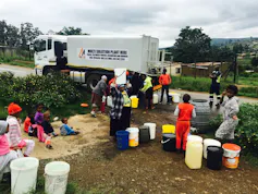 People line up with empty buckets in front of a big water truck