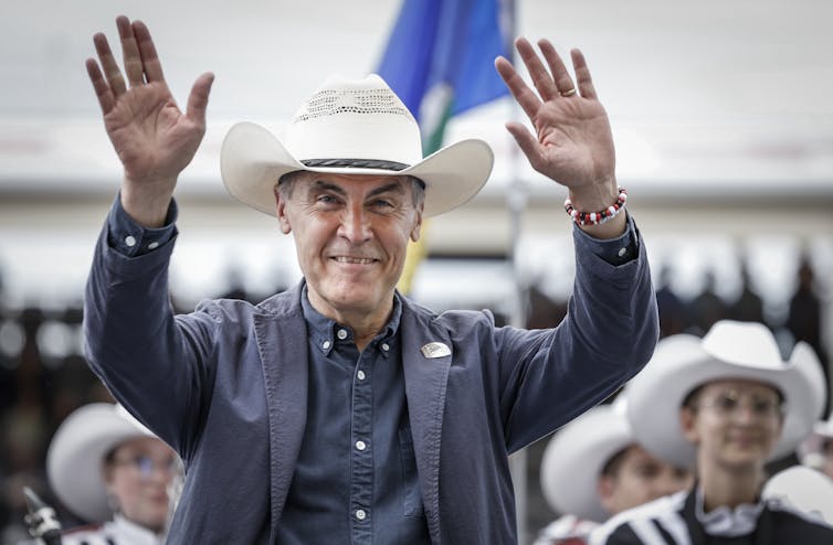 El hombre con el sombrero de vaquero está sonriendo con ambas manos.