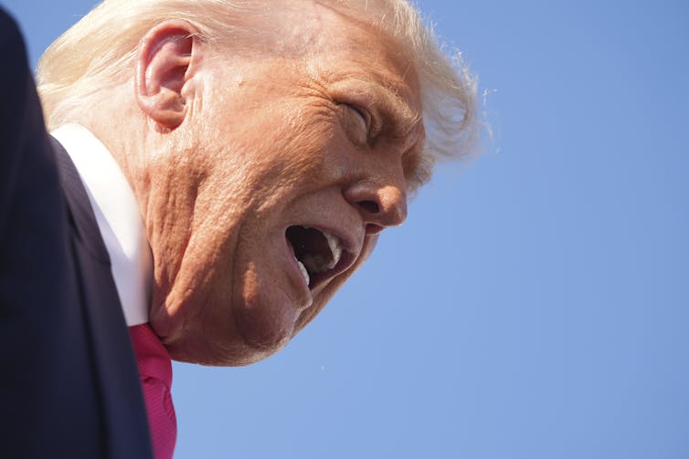 The head of a yelling man with heavy facial bronzer in silhouette.