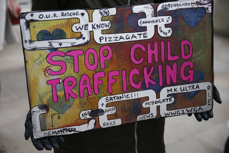 Një poster me sloganin 'Stop Child Trafficking' në shkronja të mëdha, me shkronja më të vogla që thonë 'pizzagate' dhe fraza të tjera.
