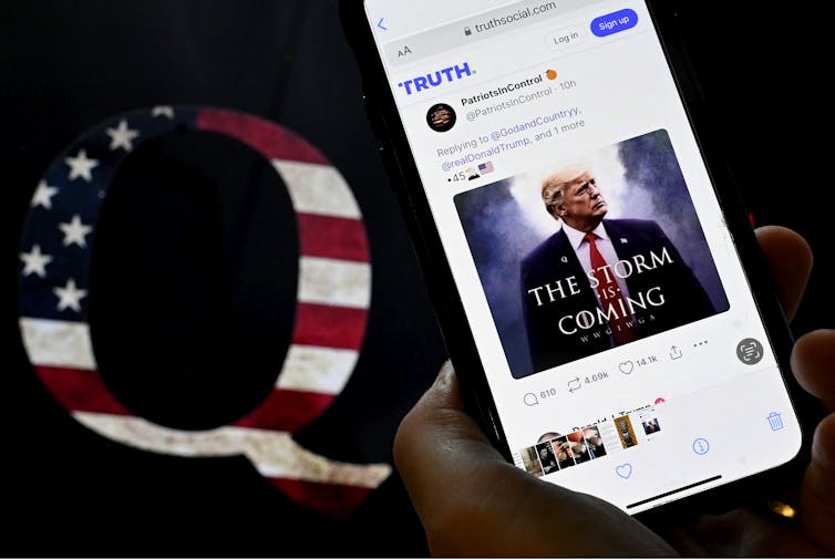 Një pajisje mobile me një imazh të Donald Trump-it pranë një sticker QAnon duke përdorur një flamur amerikan.