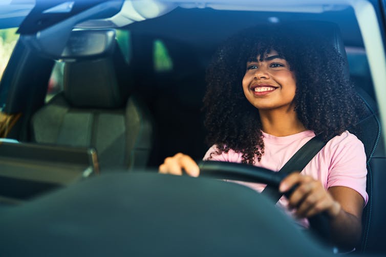 A young woman with curly smiles as she drives a car.