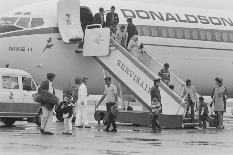 Men and women walk down stairs leading from an airplane.