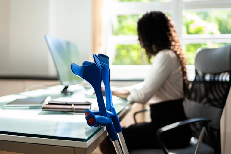 female office worker sitting at her desk alongside a set of crutches