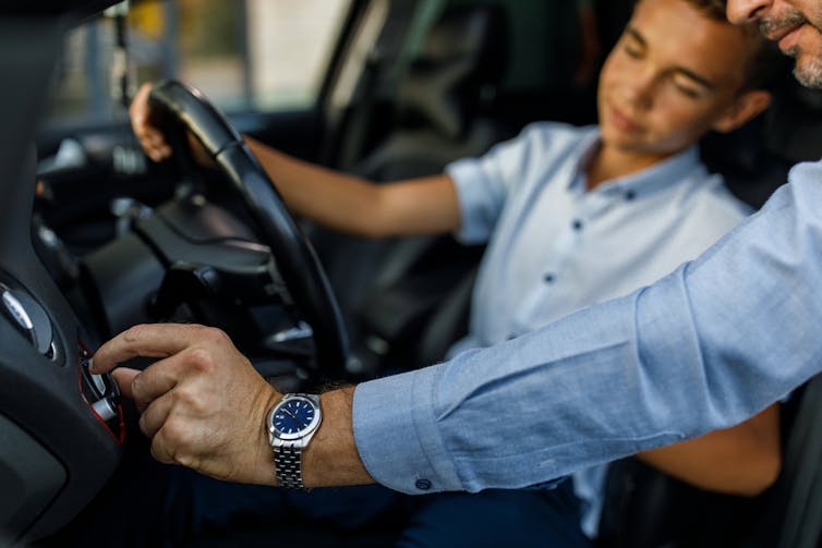 A father shows his teenage son the functions that buttons in a car performs.