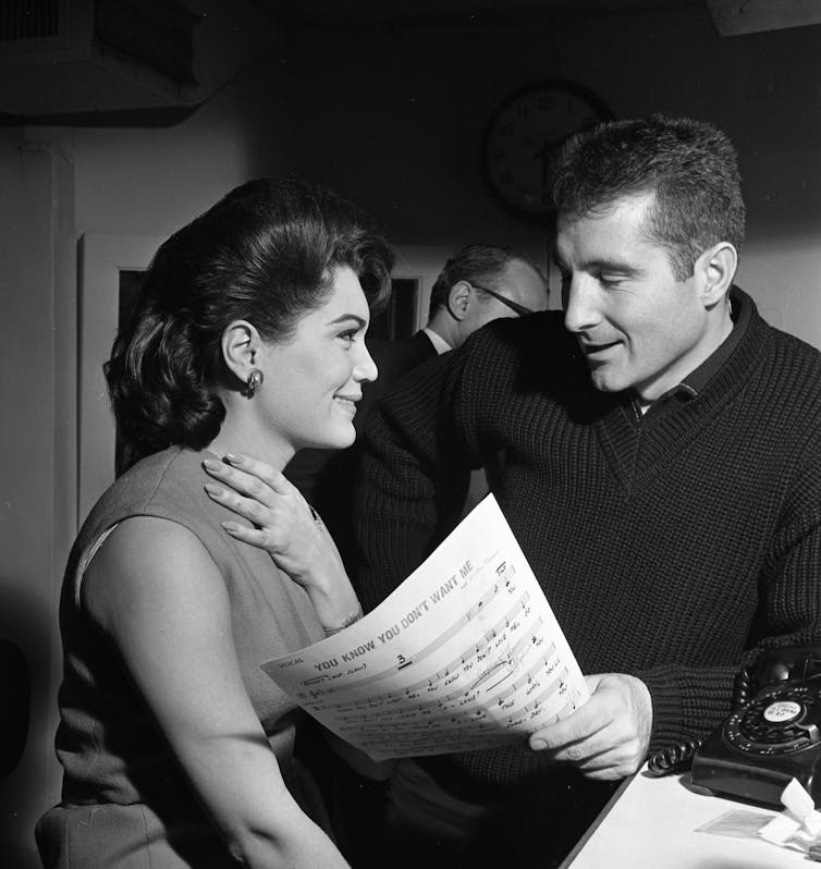 The pair look at each other, holding sheet music.