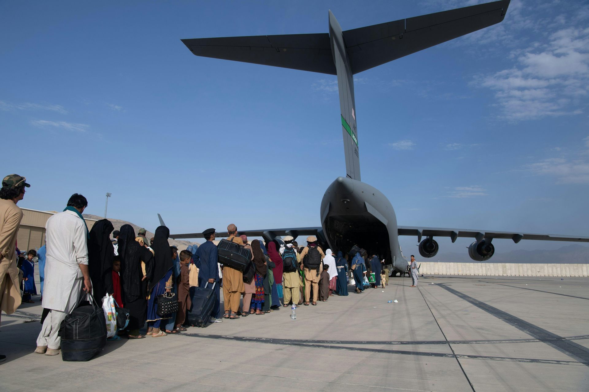 A line of people boarding a military aircraft against a blue sky