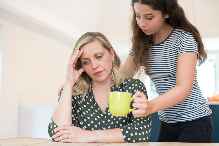 Teenage daughter offers mug of tea or coffee to unhappy looking woman