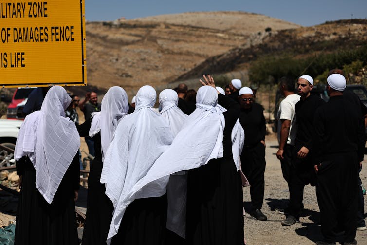 Men and women in Arab dress gather at a signpost in the Golan Heights, July 17 2025.