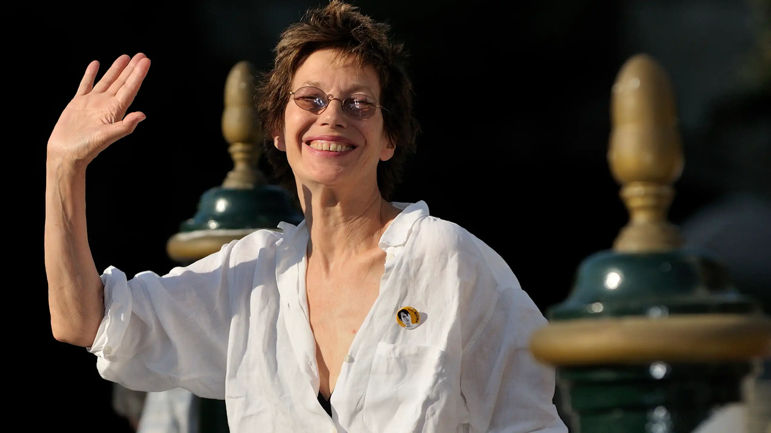 Una mujer de pelo corto sonríe a la cámara y saluda.