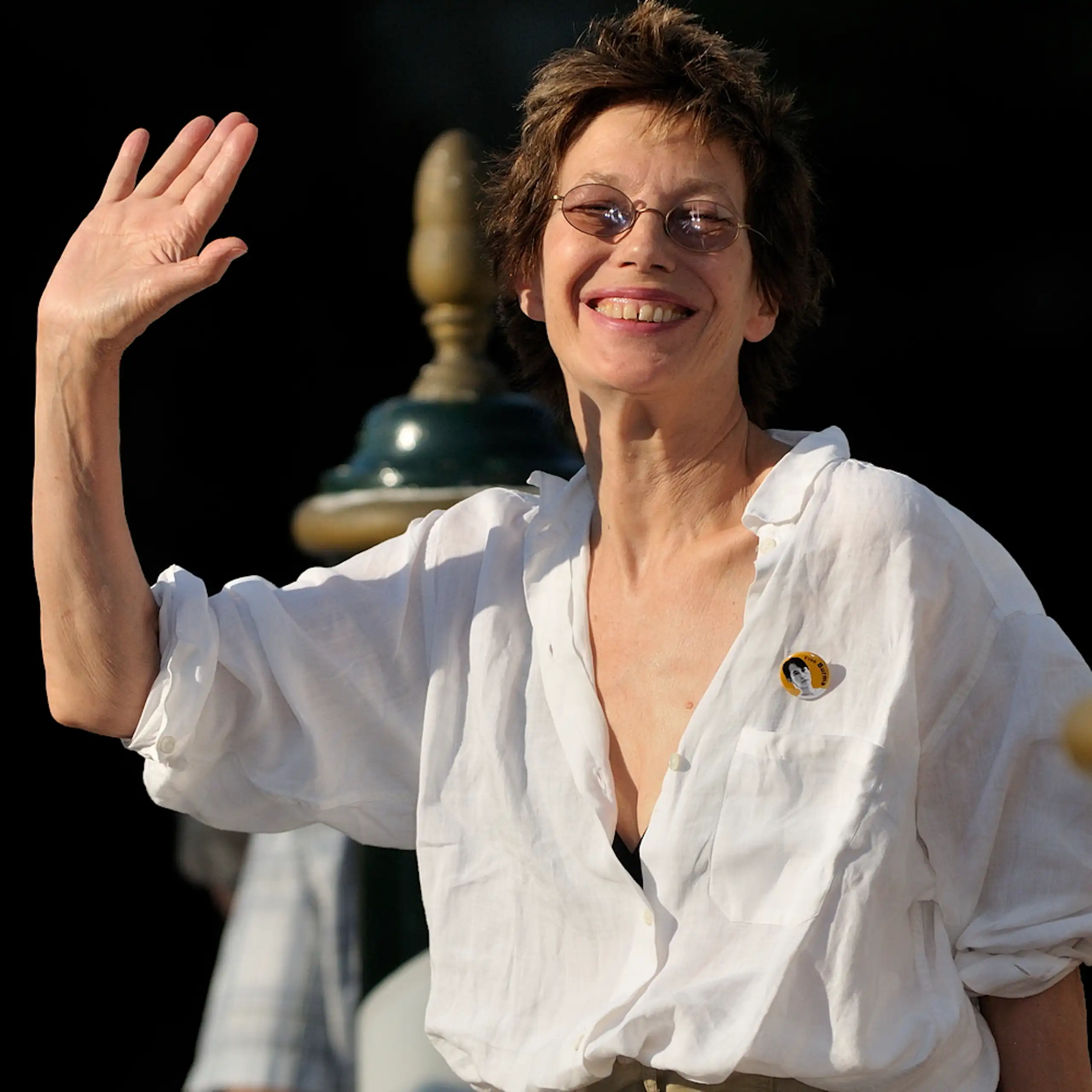 Una mujer de pelo corto sonríe a la cámara y saluda.