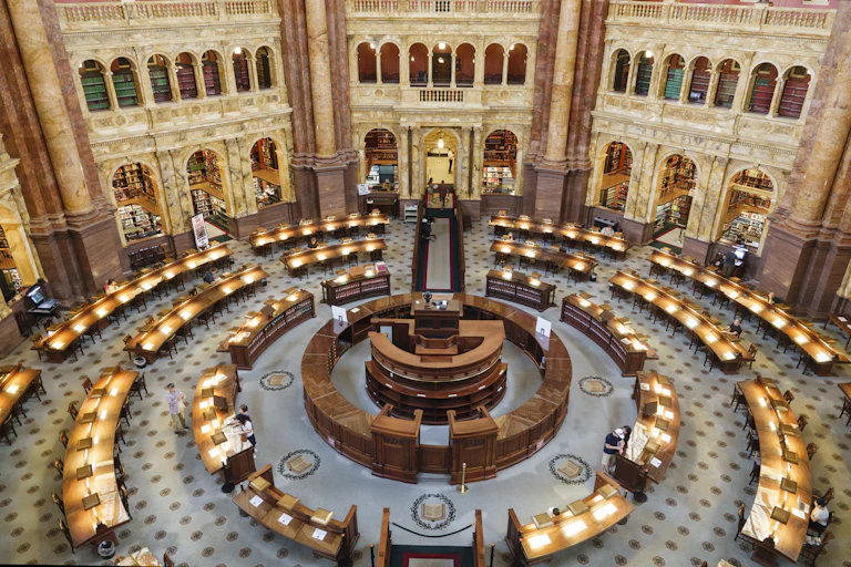 An ornate, circular room with desks and lamps on them is seen from above.