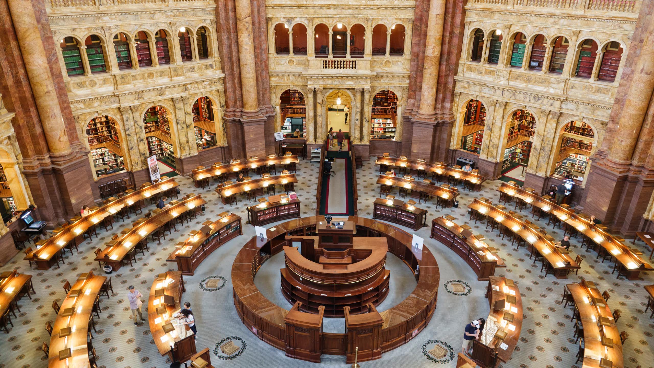An ornate, circular room with desks and lamps on them is seen from above.