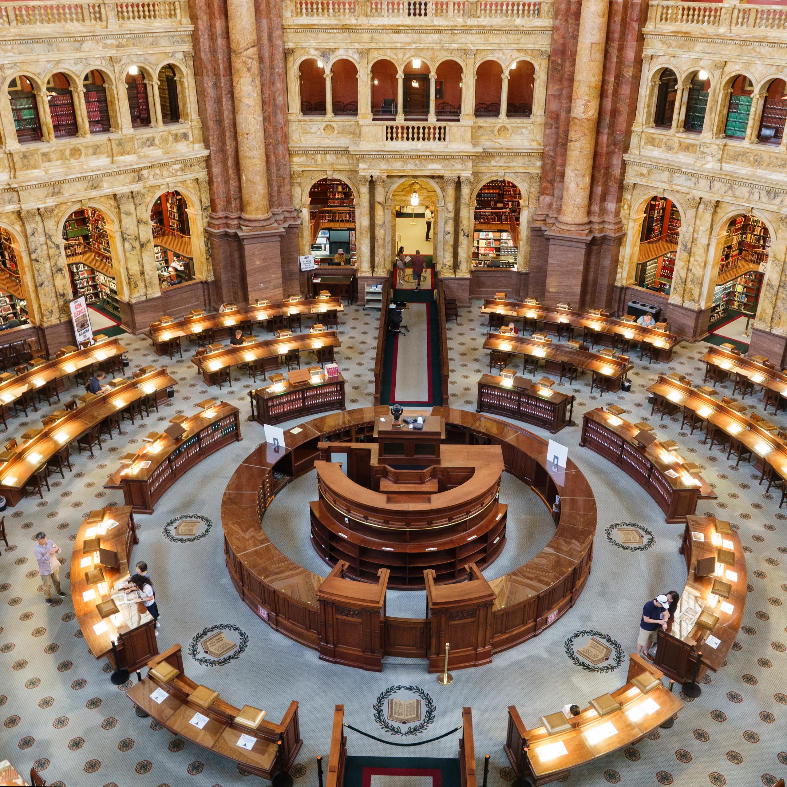An ornate, circular room with desks and lamps on them is seen from above.