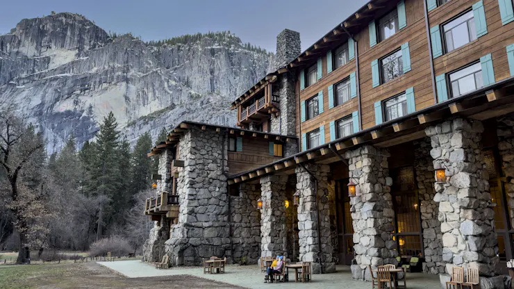 A large building stands in front of a massive set of cliffs.