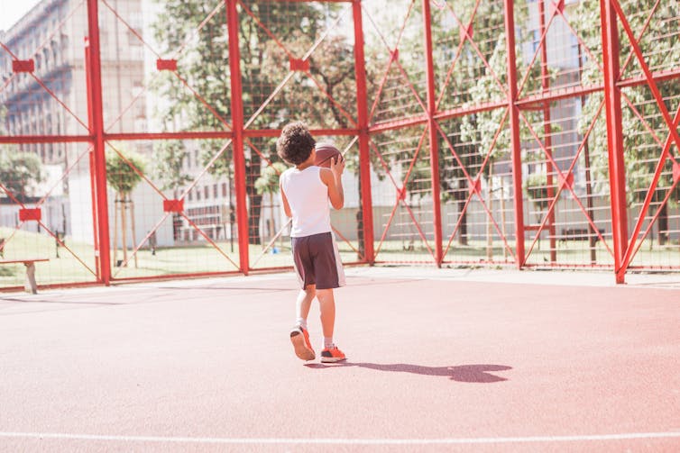 boy on empty playground holds basketball looks like he's about to shoot