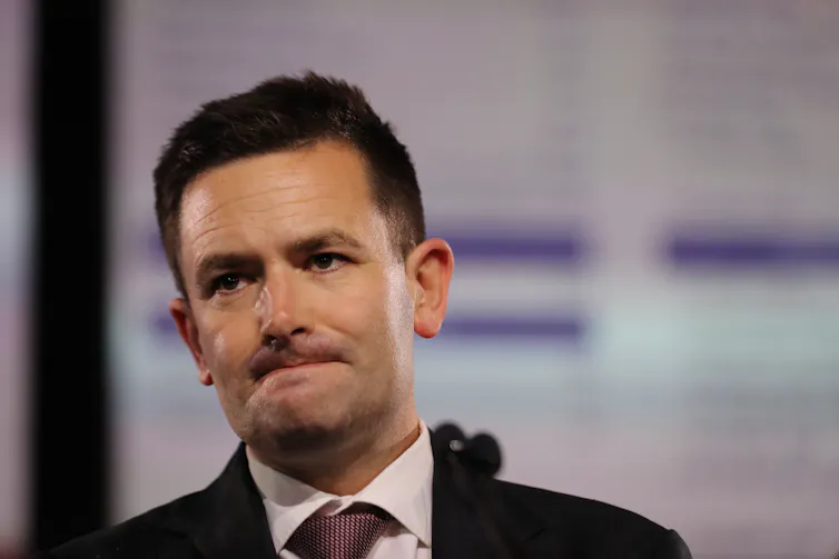 A man in a suit and tie, grimacing.