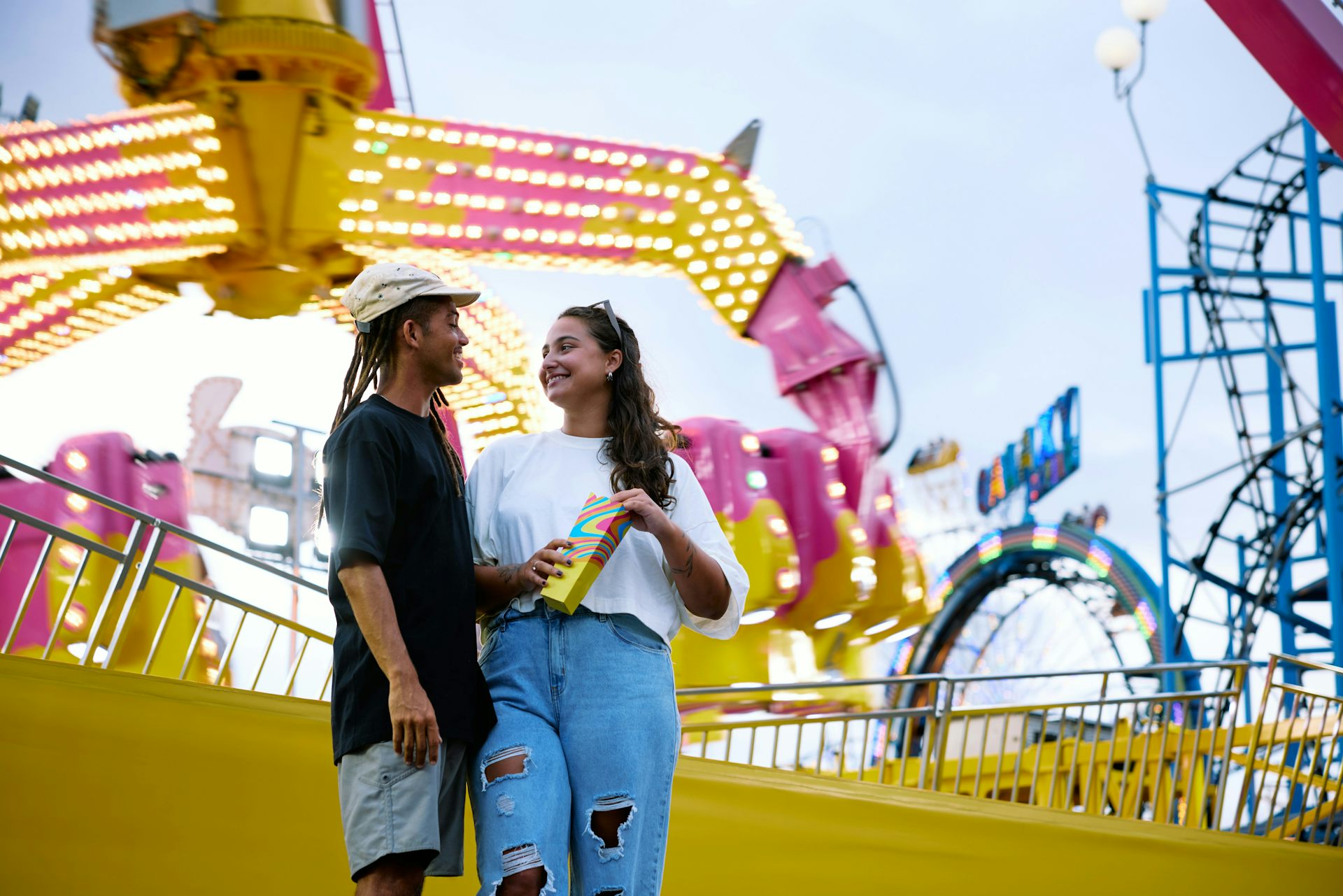 Deux jeunes gens souriants devant un manège de fête foraine.