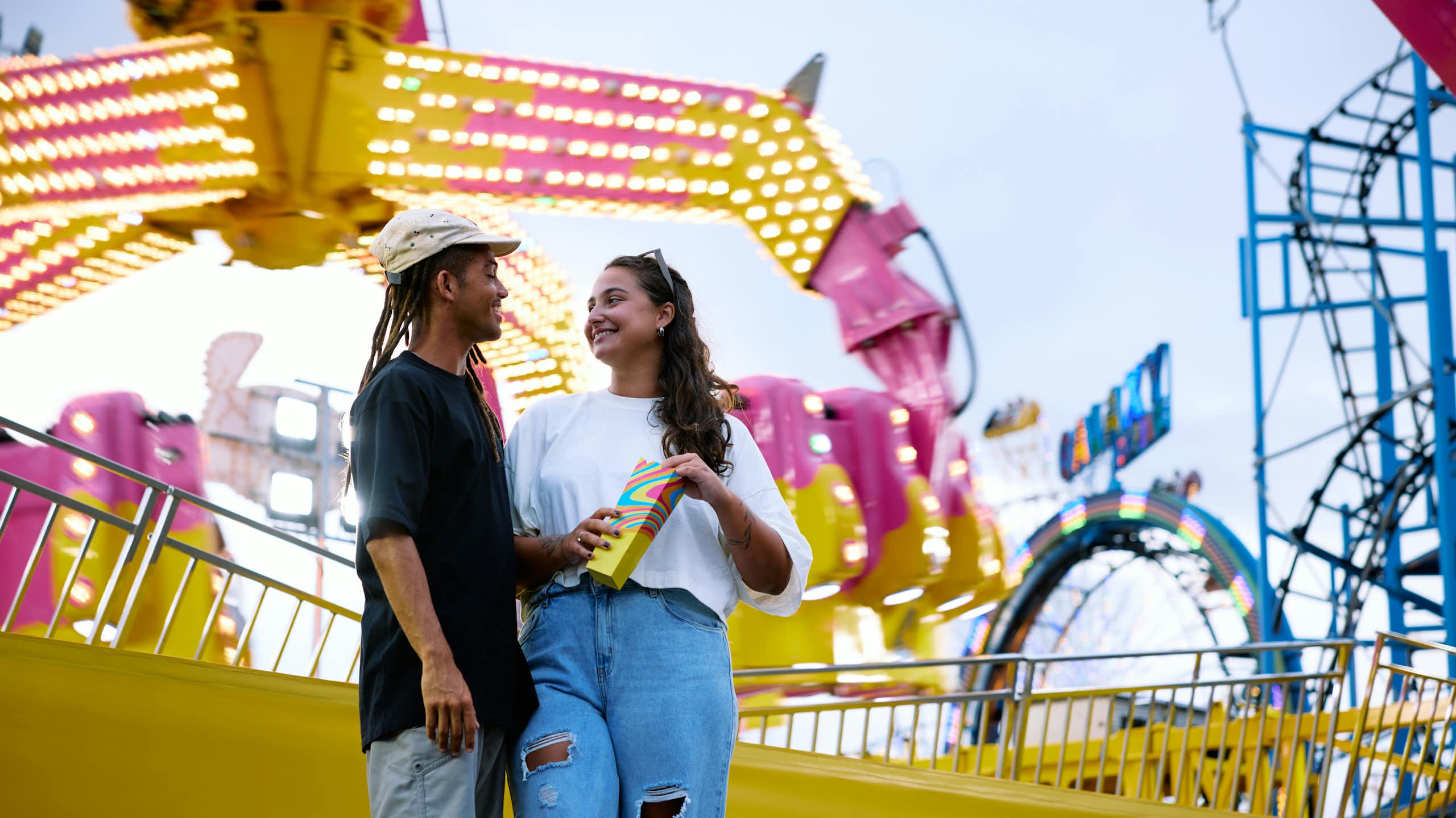 Deux jeunes gens souriants devant un manège de fête foraine.