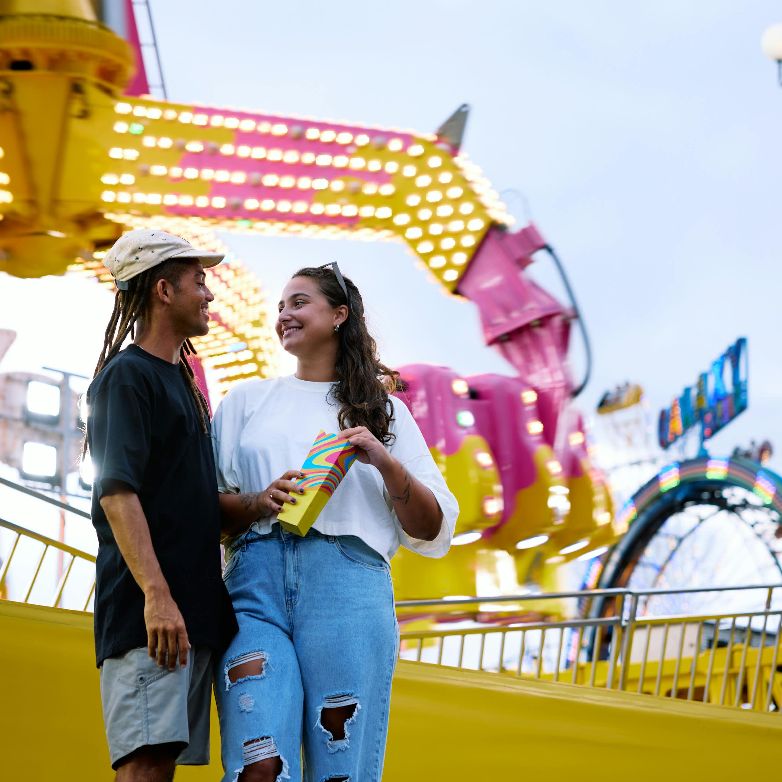 Deux jeunes gens souriants devant un manège de fête foraine.