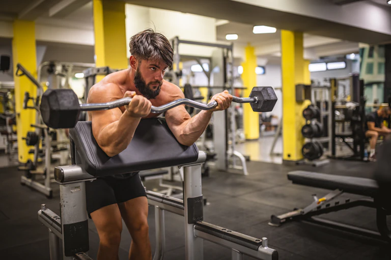 A man with large muscles lifting weights in a gym.
