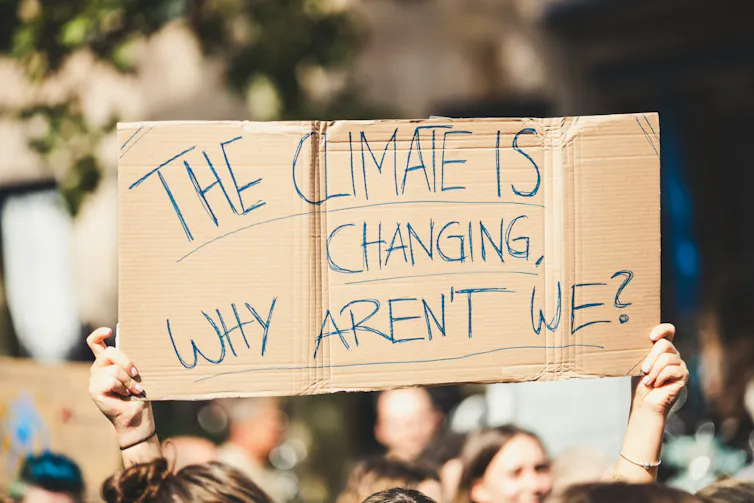 A person holds a sign that reads 'The climate is changing, why aren't we?'