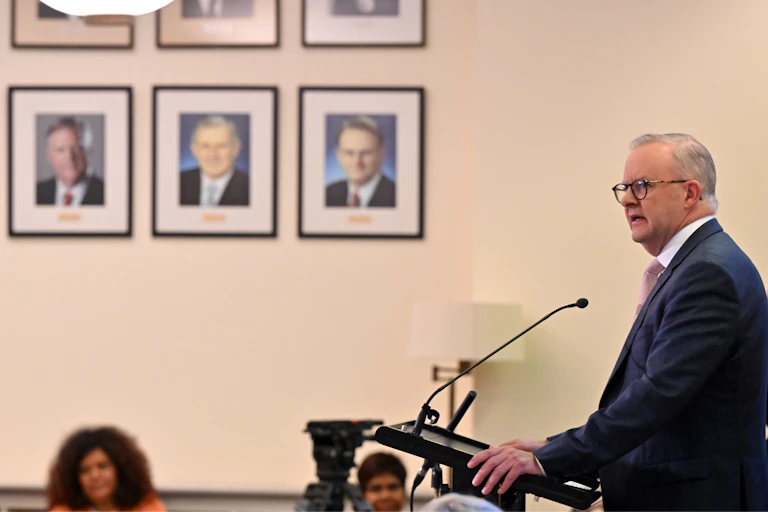 Anthony Albanese speaks to a crowd in front of a wall of portrait photos